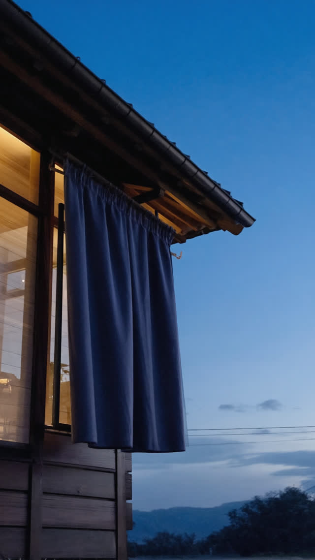 Dramatic upward view of a single noren curtain against simple wooden facade, minimalist composition, fabric as the sole subject, dusk light