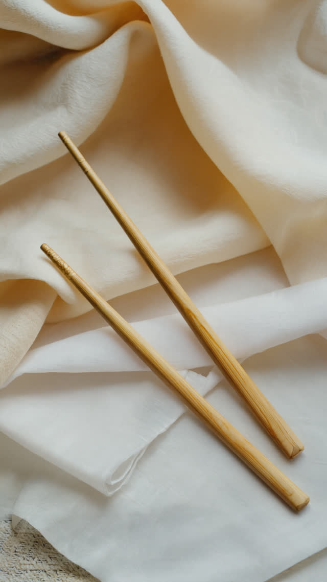 Long ceremonial chopsticks resting on folded white cloth, symbolic abstract still life, pale tones, soft diffused light, respectful minimalism