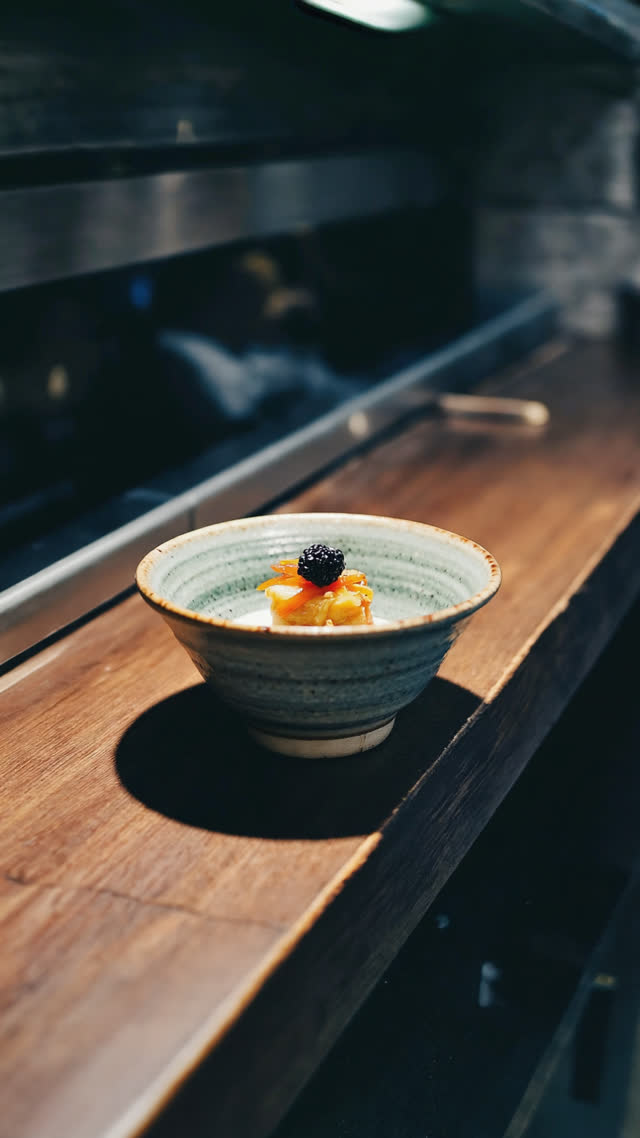Small ceramic bowl of appetizer sitting alone on a dark izakaya counter, moody spotlight, mysterious single dish, shallow depth of field