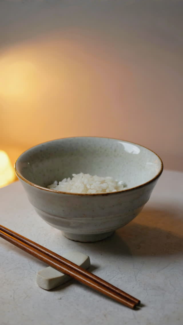 Empty rice bowl and chopsticks resting neatly on a chopstick rest after a finished meal, quiet afterglow light, close-up, still and calm